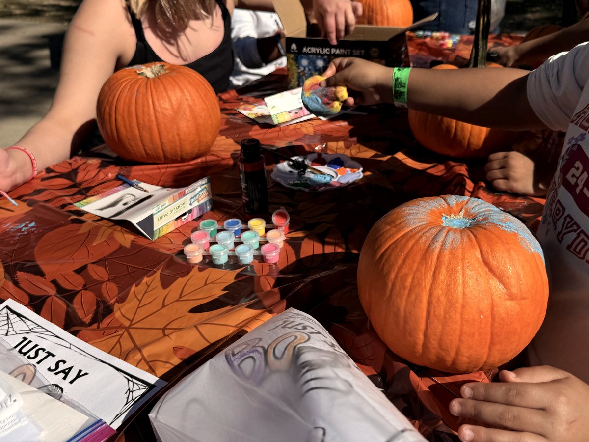 Children painting pumpkins at a Red Ribbon Spooktacular, prevention handouts on the table